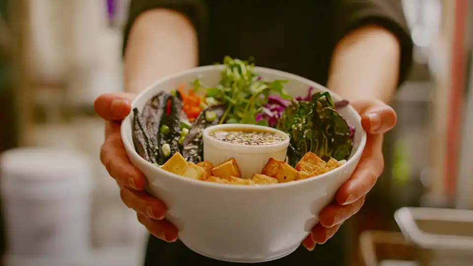 A woman holding a bowl of vegan sushi